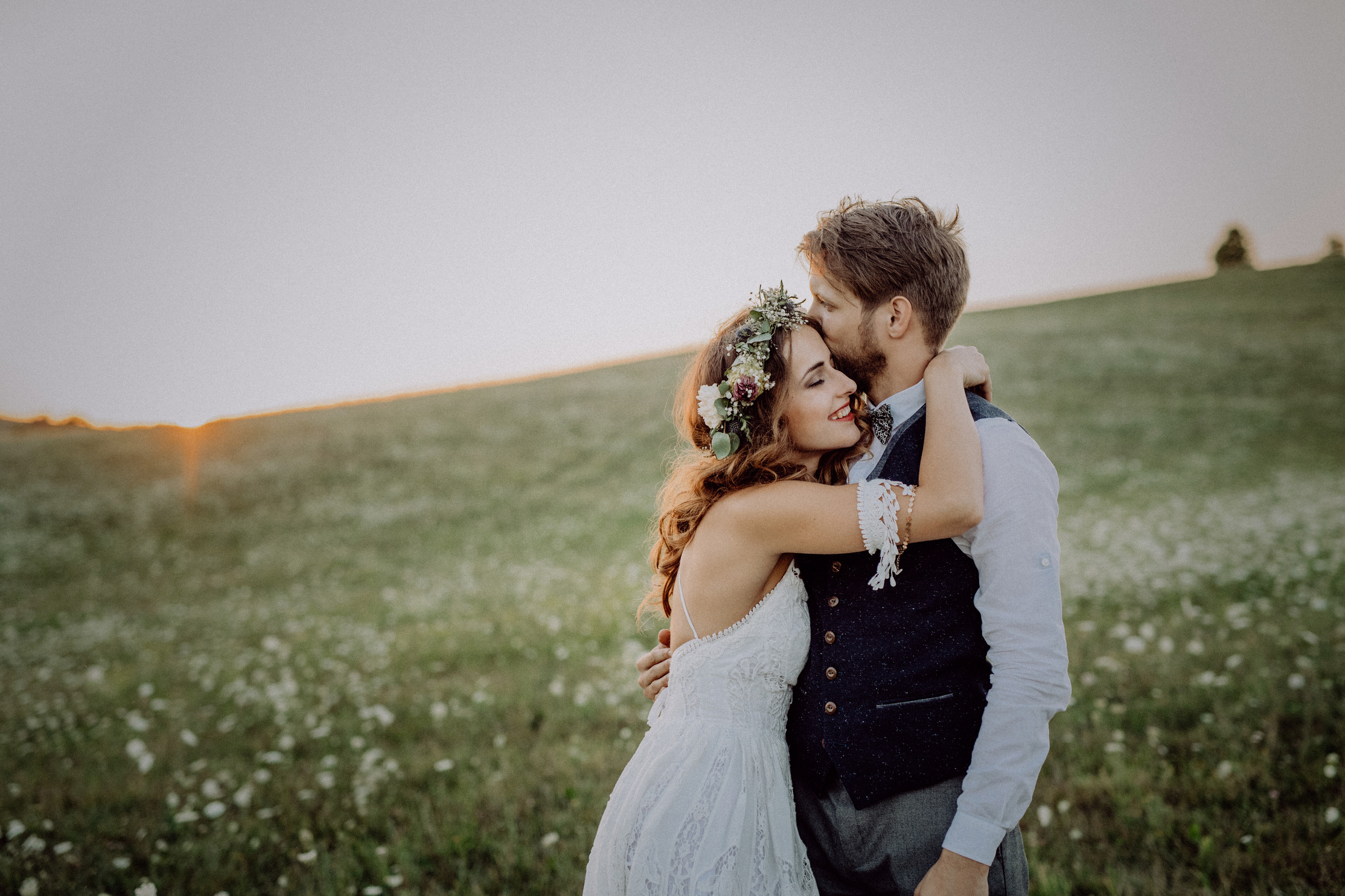 Bride and groom kissing in a field of wildflowers at sunset.  